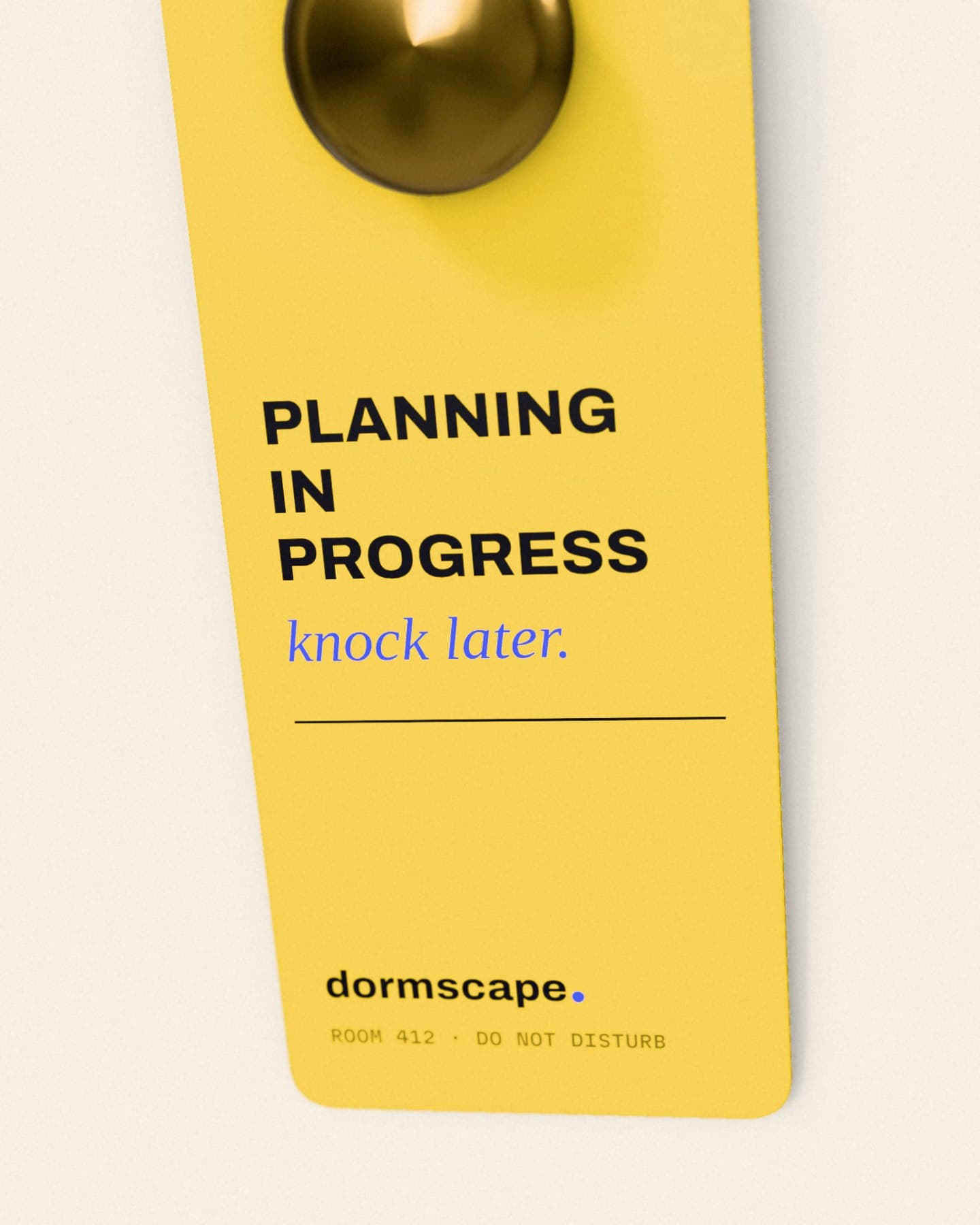 A yellow door hanger on a brass doorknob reading Planning in progress, knock later, with the dormscape logo